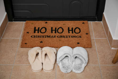 Mat with Christmas greeting and slippers near dark doorの写真素材