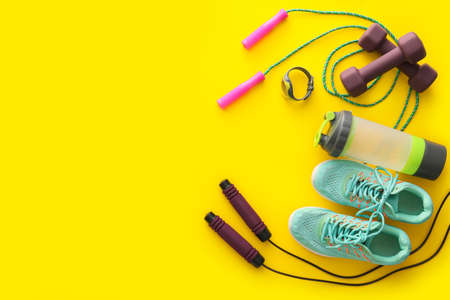 Sports equipment, bottle of water and shoes on yellow background