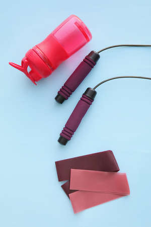 Elastic bands, skipping rope and bottle of water on color background