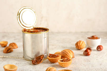 Tin can with boiled condensed milk and walnut shaped cookies on light background