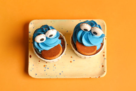 Plate with tasty funny cupcakes for Halloween celebration on orange background