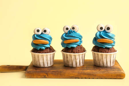 Board with tasty funny cupcakes for Halloween celebration on beige background