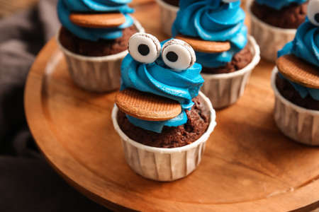 Board with tasty funny cupcakes for Halloween celebration on table, closeup