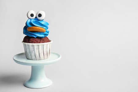 Stand with tasty funny cupcake for Halloween celebration on white background