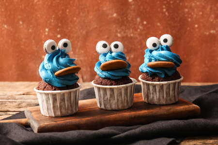 Board with tasty funny cupcakes for Halloween celebration on table