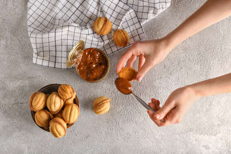 Woman preparing tasty walnut shaped cookies with boiled condensed milk on gray background