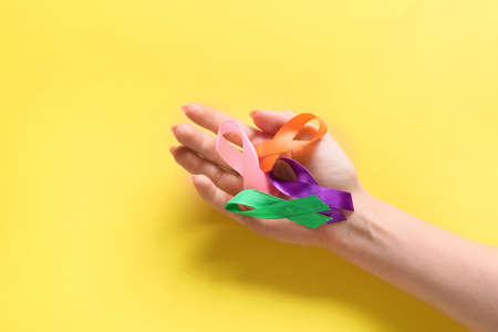 Female hand with different awareness ribbons on yellow background. World Cancer Dayの写真素材