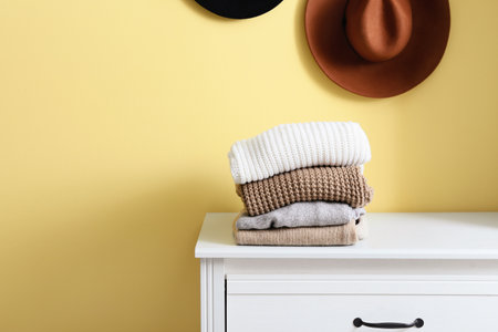 Stack of warm sweaters on commode near yellow wallの写真素材