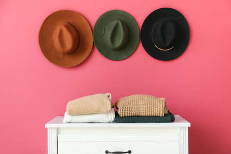 Warm sweaters on chest of drawers and stylish hats hanging on pink wallの写真素材