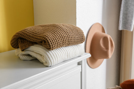 Stack of warm sweaters on shelf near yellow wallの写真素材