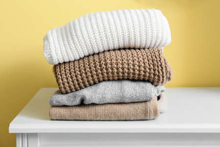 Stack of warm sweaters on shelf near yellow wallの写真素材