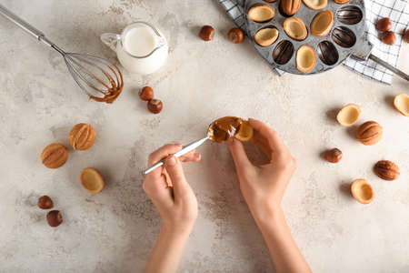 Woman preparing tasty walnut shaped cookies with boiled condensed milk on light backgroundの写真素材