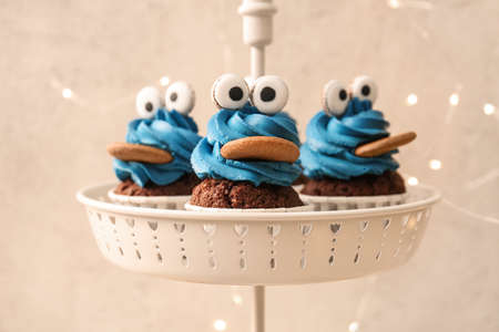 Stand with tasty funny cupcakes for Halloween celebration on light background