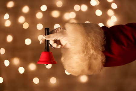 Santa hand with Christmas bell against blurred lightsの写真素材
