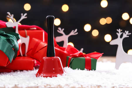 Red Christmas bell on table with snow and gifts on backgroundの写真素材