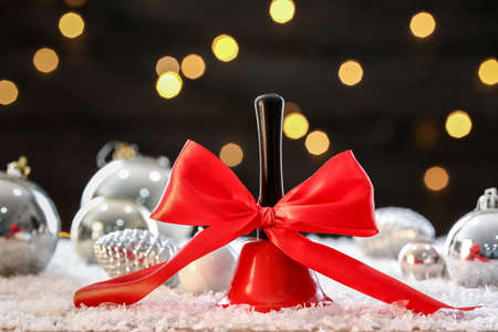 Red Christmas bell and beautiful decorations on table with snow against blurred lights