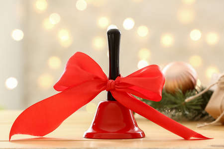 Christmas bell with red ribbon on table against blurred lightsの写真素材