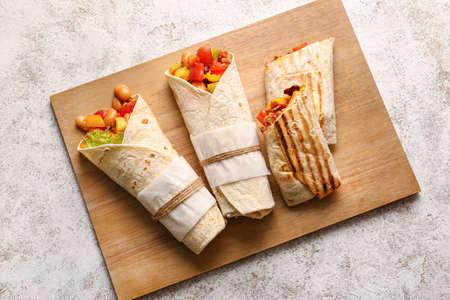Board of tasty Mexican burritos with vegetables on light backgroundの写真素材