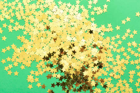 Heap of golden confetti in shape of stars on color background, closeup