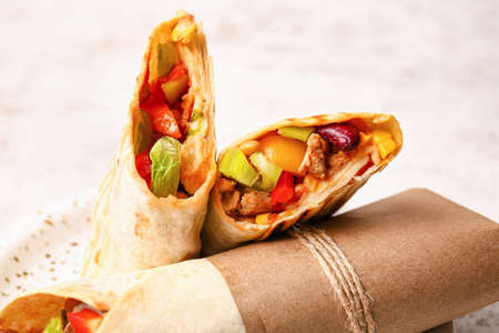 Tasty Mexican burritos with vegetables on light background, closeup