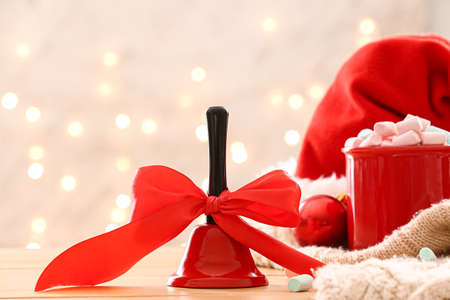 Christmas bell with red ribbon on table against blurred lightsの写真素材