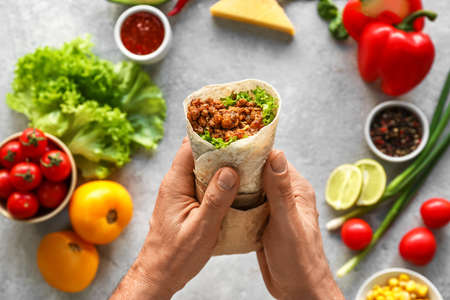 Man with tasty burrito and ingredients on gray backgroundの写真素材
