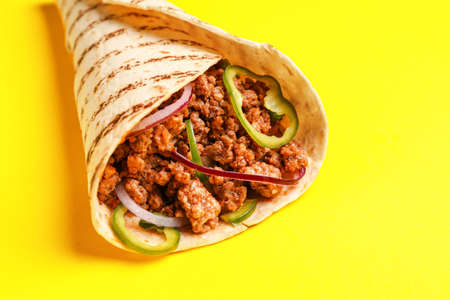 Tasty burrito on yellow background, closeup