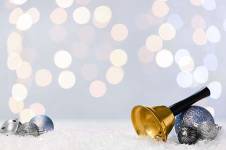 Golden Christmas bell and decorations on snow against blurred lightsの写真素材