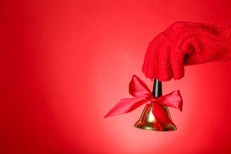 Female hand in knitted glove with Christmas bell on red background, closeupの写真素材