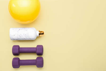 Stylish dumbbells, bottle and ball on yellow background