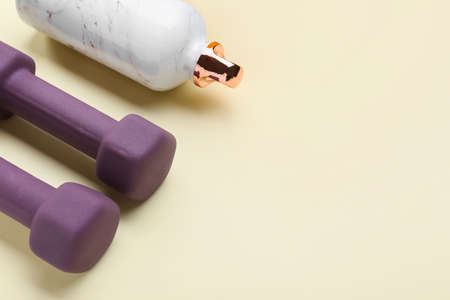 Stylish dumbbells and bottle on yellow backgroundの写真素材
