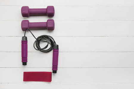 Stylish dumbbells, elastic band and skipping rope on light wooden background