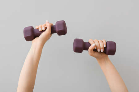 Female hands with stylish dumbbell on light background