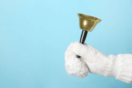 Female hand in knitted mitten with Christmas bell on color background, closeupの写真素材