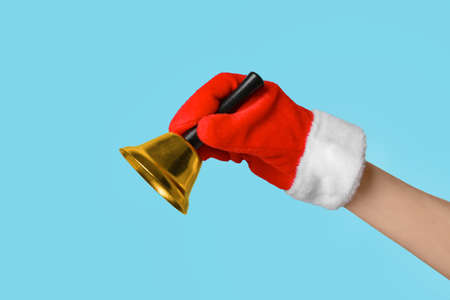 Female hand in Santa mitten with Christmas bell on color background, closeupの写真素材