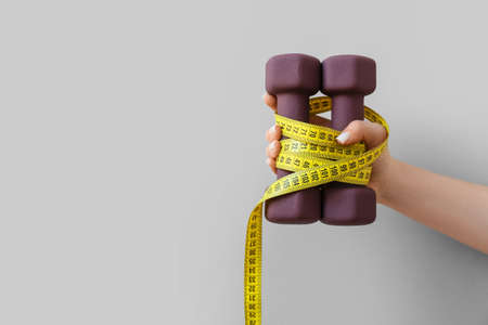 Female hand with stylish dumbbells and measuring tape on light backgroundの写真素材