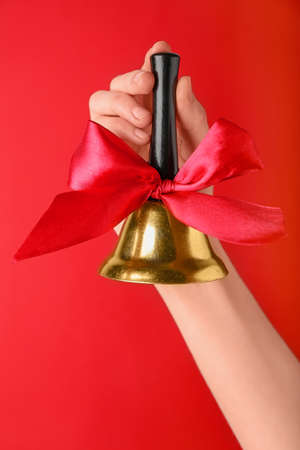 Woman holding golden Christmas bell on red background, closeup