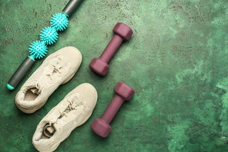 Stylish dumbbells, massage roller and shoes on green background