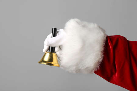 Santa Claus holding golden Christmas bell on gray background, closeupの写真素材