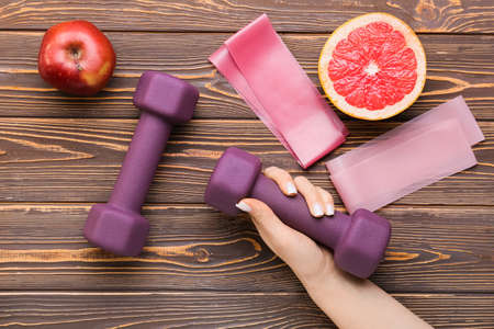 Female hand with stylish dumbbells on wooden background