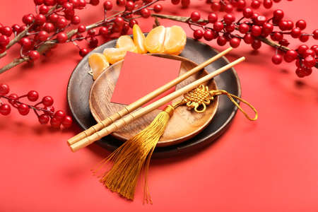 Plates with empty greeting card, chopsticks, tangerines and Chinese amulet on color backgroundの写真素材