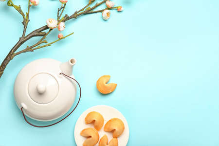 Plate with fortune cookies, teapot and blooming tree branch on color backgroundの写真素材