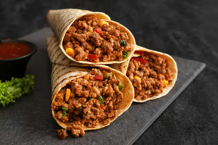 Slate plate with tasty burritos and sauce on dark background, closeupの写真素材