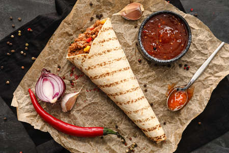 Parchment with tasty burrito, sauce and spices on dark backgroundの写真素材
