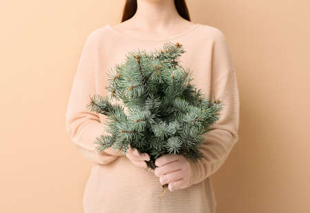 Young woman with fir tree branches on beige backgroundの写真素材