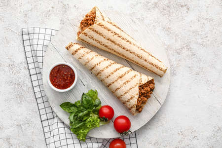 Board with tasty burritos and sauce on light background