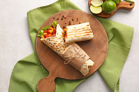 Board with delicious burritos and lime on light backgroundの写真素材