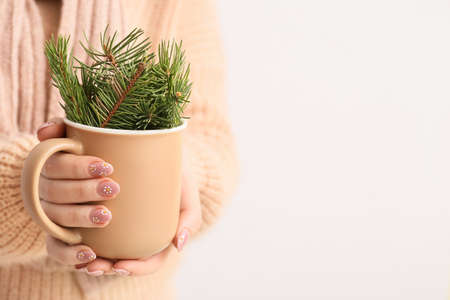 Young woman holding cup with fir tree branches on light background, closeupの写真素材