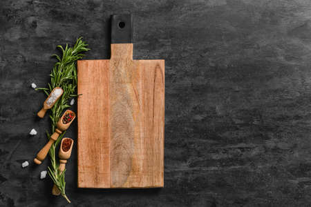 Wooden cutting board and spoons with spices on dark background