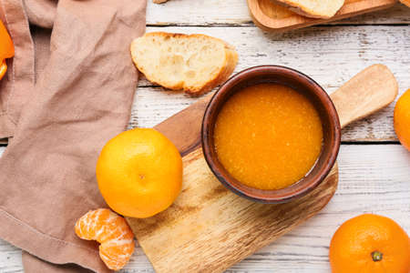 Board with bowl of tasty tangerine jam on light wooden backgroundの写真素材